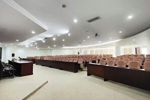A conference room with rows of chairs, a podium, and a carpeted floor. - Kant's Apartment Hotel (Zhuhai)