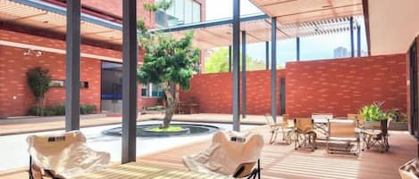 Un espace extérieur aménagé avec des tables et des chaises, un petit arbre et, au fond, un bâtiment en briques.
