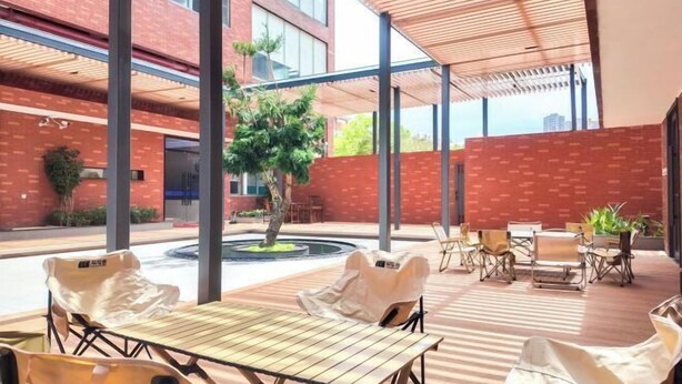 Un espace extérieur aménagé avec des tables et des chaises, une partie abritée et un petit arbre.