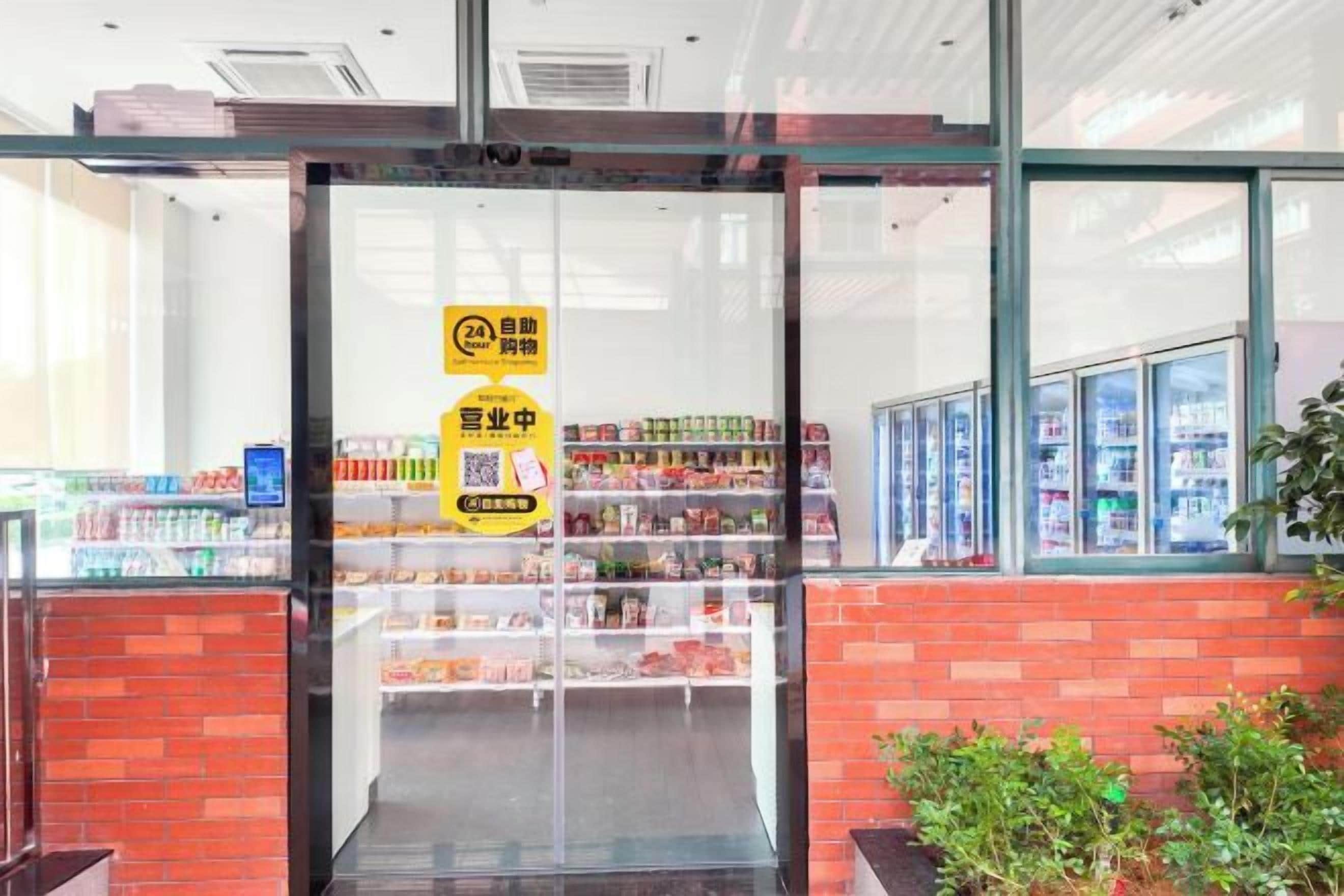 Entrada de una tienda con puerta de vidrio, un cartel con un código QR y estantes llenos de productos.