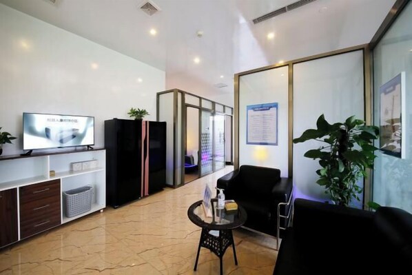 A modern lobby with a flat-screen TV, a reception desk, a black leather sofa, a small round table, and a potted plant. - Kant's Apartment Hotel (Zhuhai)
