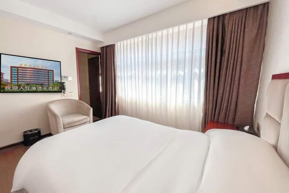 Hotellihuone, jossa on suuri sänky, tuoli, televisio ja ikkuna, jossa on verhot.