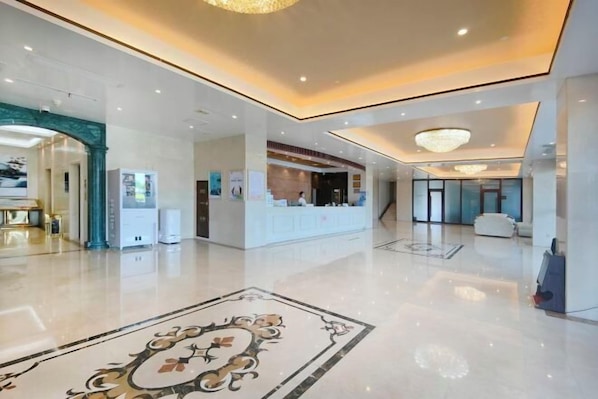 A spacious lobby with a polished floor, a reception desk, and a large decorative rug.