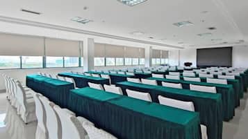 A conference room with rows of tables and chairs, large windows, and a projection screen.
