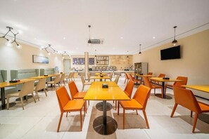 A modern dining area with multiple tables and chairs, a flat-screen TV mounted on the wall, and a ceiling with pendant lighting.
