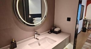 Un baño moderno con un espejo redondo, un lavabo y una pequeña zona de tocador.