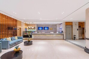 A hotel lobby with a reception desk, seating area, and a staircase leading to an elevator.