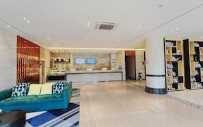 Un hall de hotel con una recepción, un sofá, una mesa de centro y una estantería.