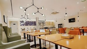A modern dining area with tables and chairs, a kitchen in the background, and a TV mounted on the wall. - City Comfort Inn (Dali)