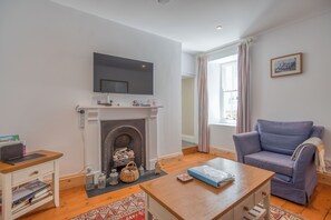 Una sala de estar con chimenea, un televisor montado encima, un sofá azul y una mesa de centro de madera.