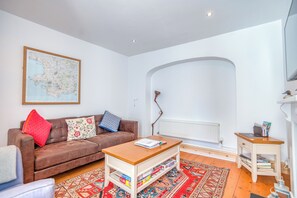 A living room with a brown sofa, a wooden coffee table, a patterned rug, a white radiator, and a framed map on the wall. - Delfryn, Holiday Cottage Manorbier, Sleeps 4, 2 bedrooms,  bathrooms (Tenby)