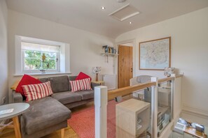 Un salon avec un canapé gris, des coussins rouges et blancs, une petite table, un radiateur, une bibliothèque et une carte accrochée au mur.
