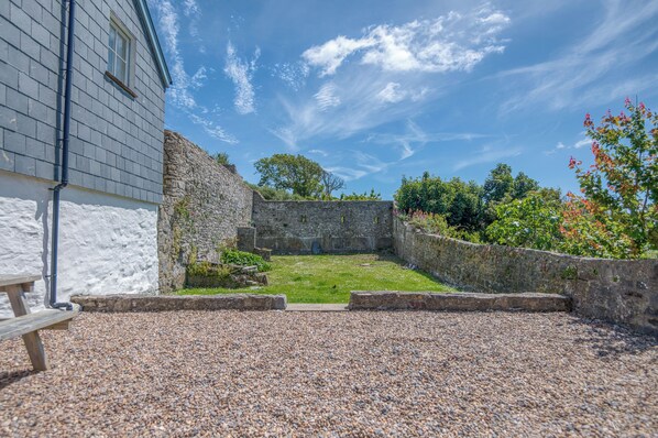 A courtyard with a stone wall, a grassy area, and a building with a window.