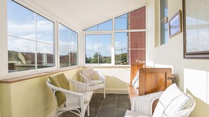 A sunlit room with large windows, wicker furniture, and a view of greenery. - Harbour View, Holiday Cottage Porthgain, Sleeps 10, 5 bedrooms,  bathrooms (Haverfordwest)