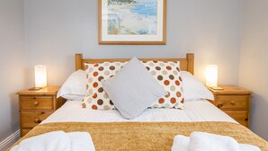 A neatly made bed with a polka dot pillow, a framed painting above, and bedside lamps on wooden nightstands. - Harbour View, Holiday Cottage Porthgain, Sleeps 10, 5 bedrooms,  bathrooms (Haverfordwest)