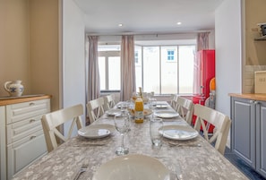 A dining area with a table set for four, chairs, a vase, and a bottle of orange juice. - Ty Mor, Holiday Cottage Manorbier, Sleeps 8, 4 bedrooms,  bathrooms (Tenby)