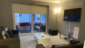A modern living room with a sofa, a coffee table, and a TV mounted on the wall. - 1-bedroom Apartment Sleeps 4, Parking (Hythe)