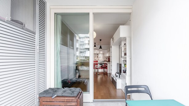 Ein modernes Interieur mit einer Holzbank, einem Türkis-Tisch und einem durch eine offene Tür einsehbaren Küchenbereich.