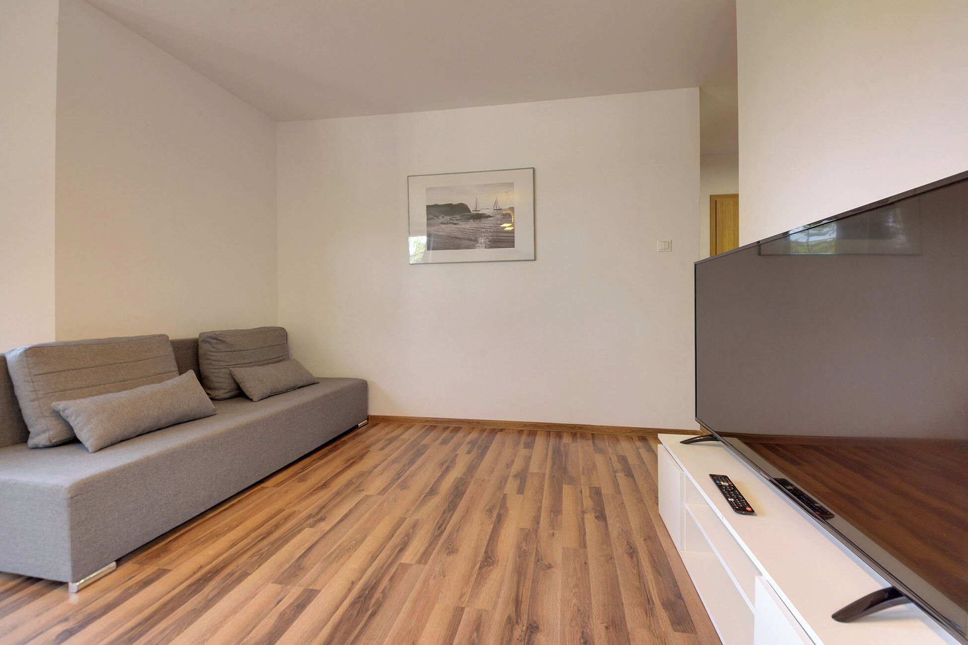 Una sala de estar moderna con un sofá gris, un televisor de pantalla plana y un cuadro en la pared.