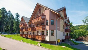 A multi-story chalet with wooden balconies, a paved driveway, and a lush green landscape. - RentPlanet - Apartamenty Nadrzeczna (Karpacz)