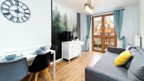 A modern living room with a grey sofa, a dining table with chairs, a white dresser, and a large wall clock. - RentPlanet - Apartamenty Nadrzeczna (Karpacz)