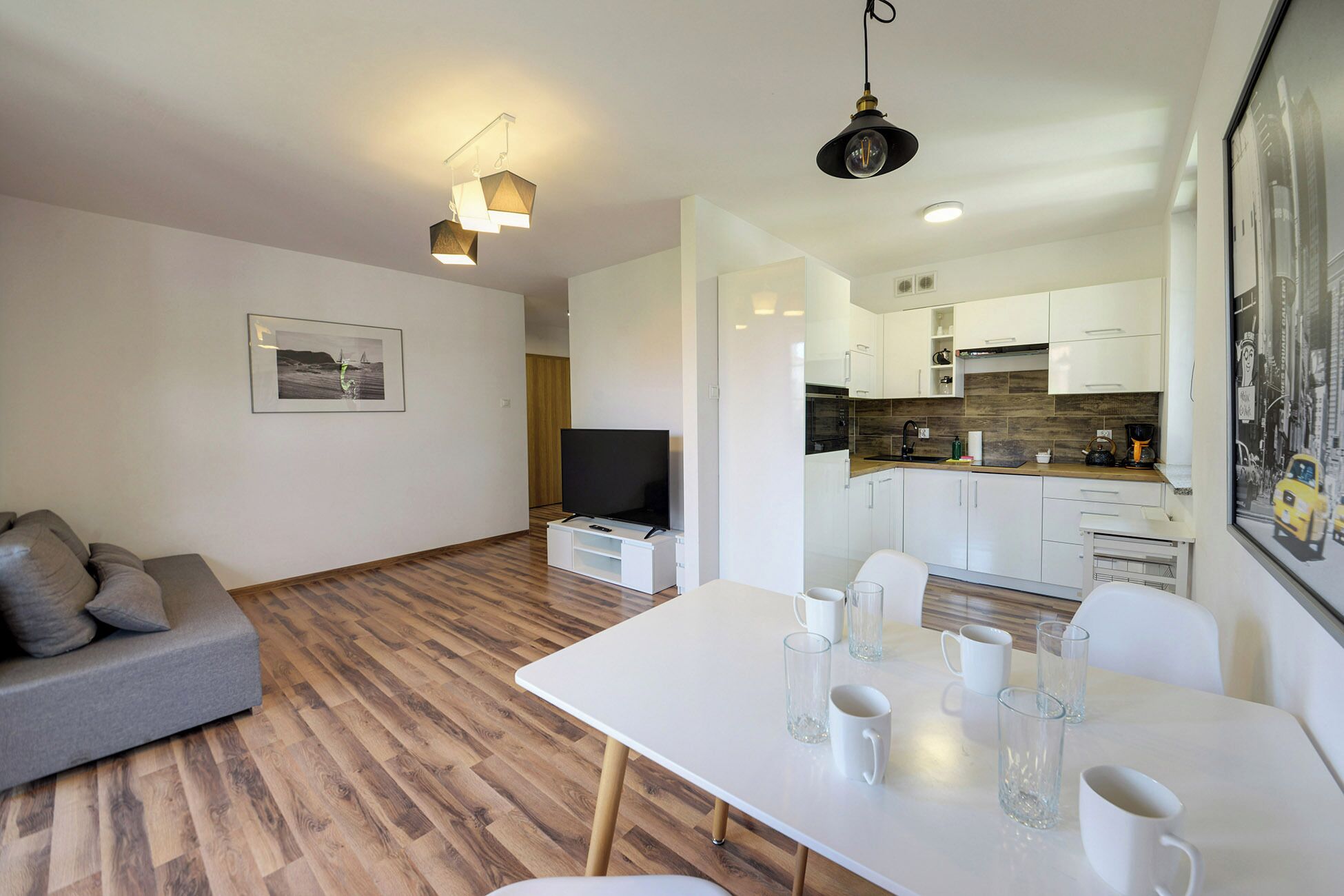 A modern living room with a sofa, a dining table with glasses, and a TV.