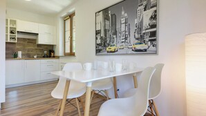 A modern kitchen with white cabinets, a wooden countertop, and a dining area with a white table and chairs. A cityscape painting is on the wall. - RentPlanet - Apartamenty Nadrzeczna (Karpacz)