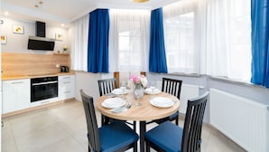 A modern kitchen with a built-in oven, a coffee maker, and a dining area with a round table set for four. - Apartamenty Sun & Snow Nad Łomnicą (Karpacz)