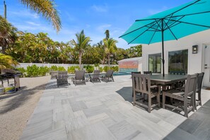 A patio area with a table and chairs, a blue umbrella, and a grill. - White Palms by Beach Boutique Rentals (Anna Maria)