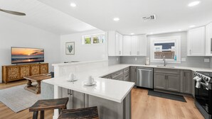 Une cuisine moderne avec des meubles blancs, un îlot central et un coin repas doté de chaises en bois.