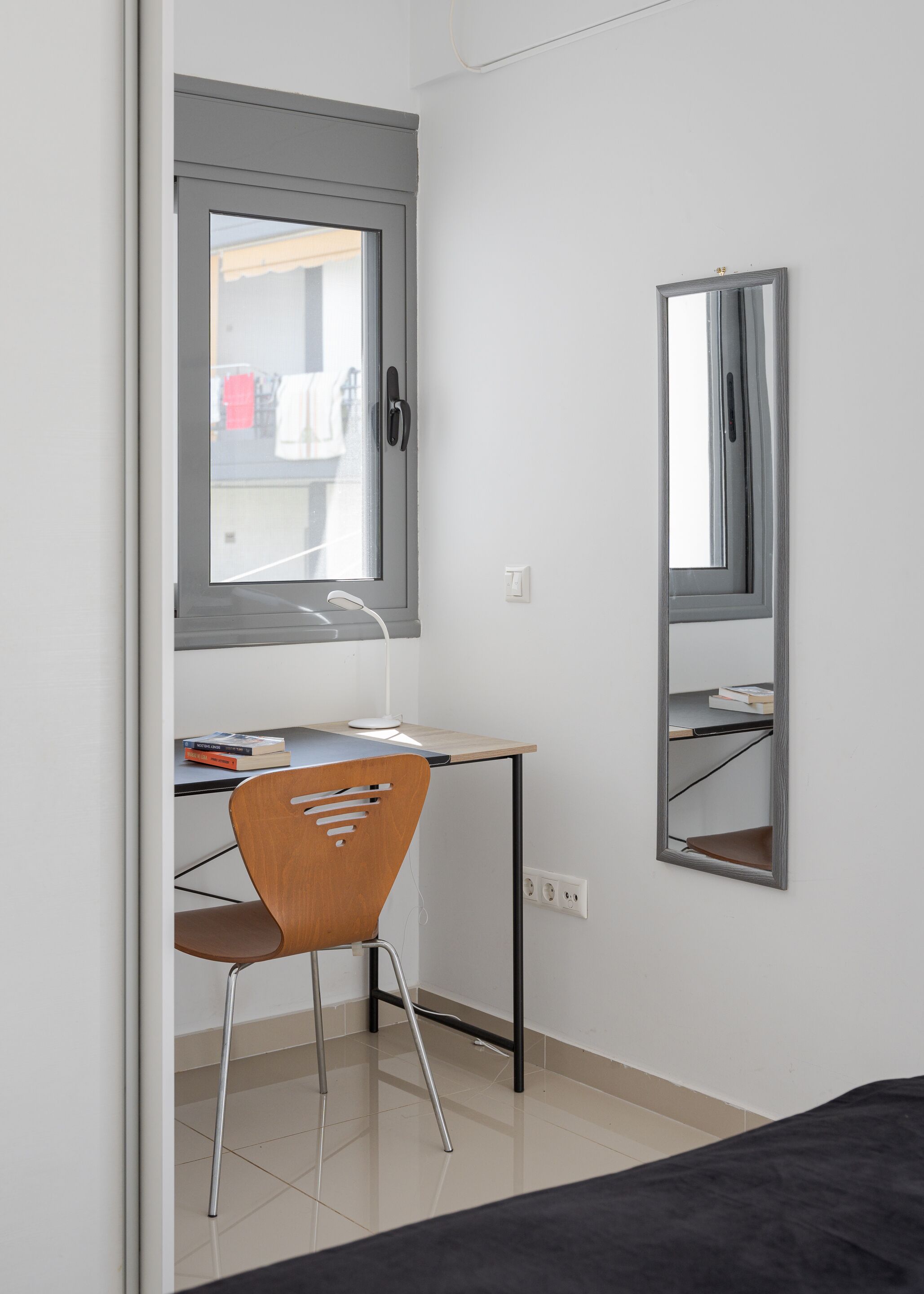 A small, modern room with a desk, chair, and a large mirror.