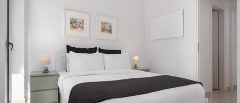 Quarto moderno com uma cama grande, duas mesas de cabeceira com luminárias e duas imagens emolduradas na parede.