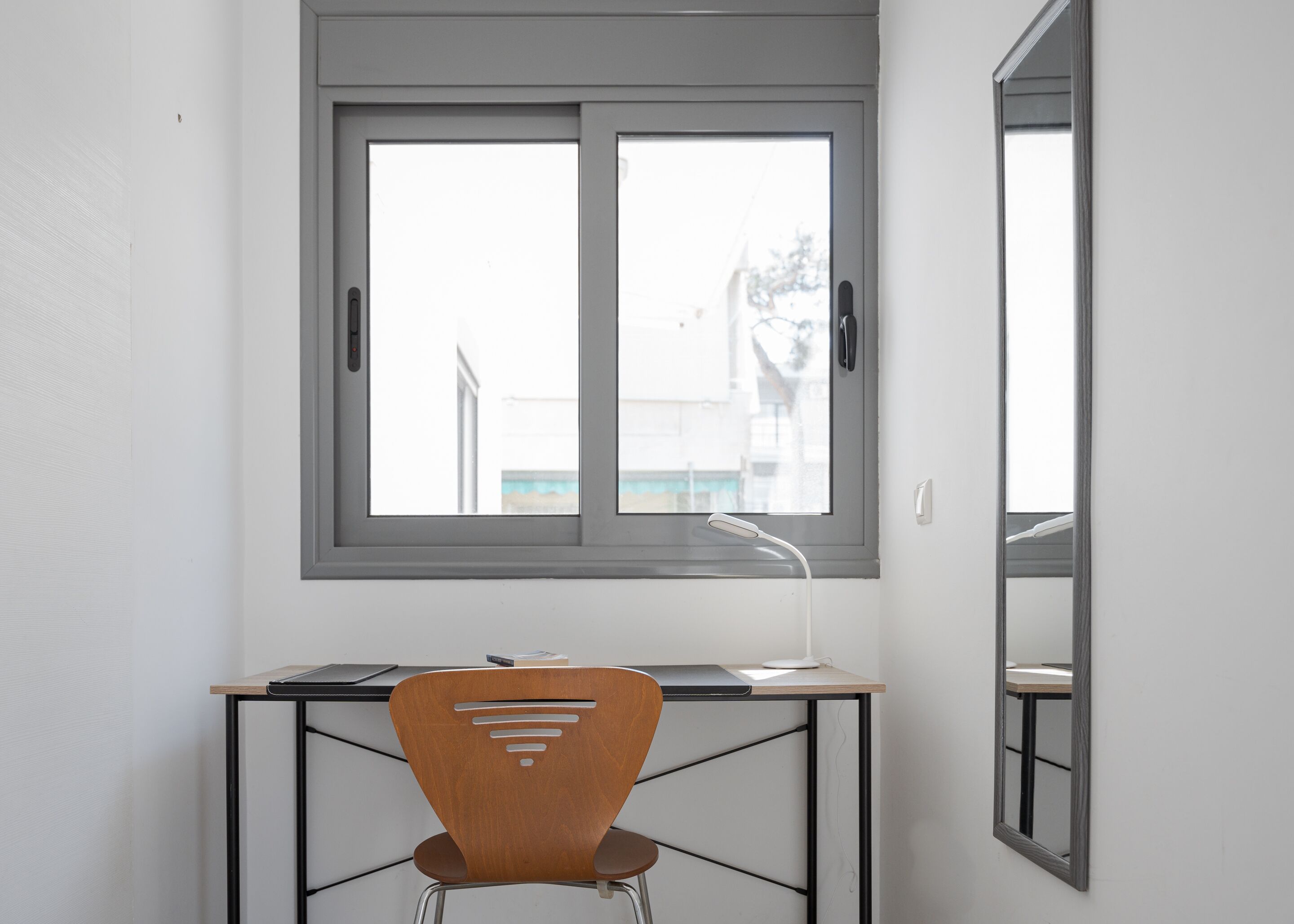 Una habitación con escritorio, silla y ventana con vistas a edificios.