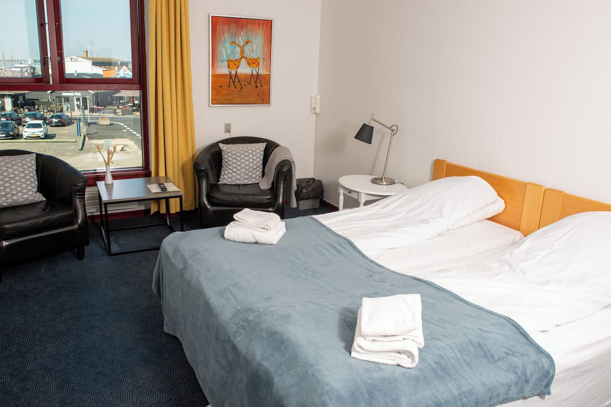 A hotel room with a bed, a chair, a desk, a lamp, and a painting on the wall.