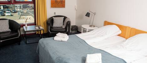 A hotel room with a bed, a chair, a desk, a lamp, and a painting on the wall.