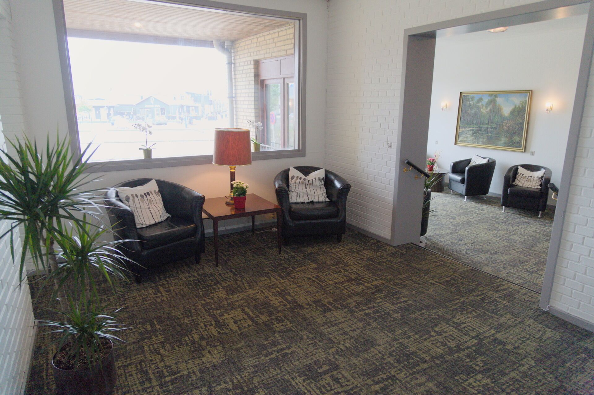 A room with a large window, two leather chairs, a small table with a lamp, and a potted plant.