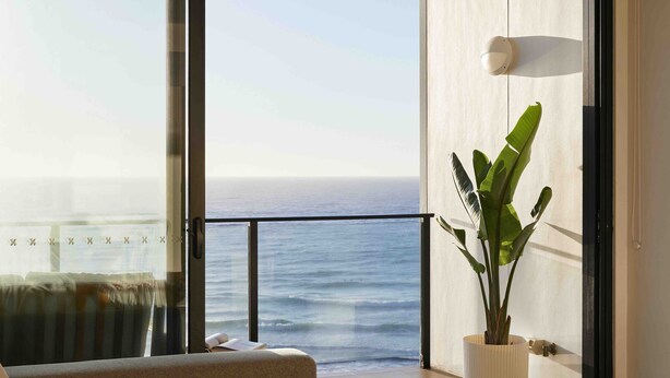 A balcony with a view of the ocean, a potted plant, and a modern light fixture.