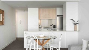 A modern kitchen with white cabinetry, a central island with a glass top table, and white chairs.