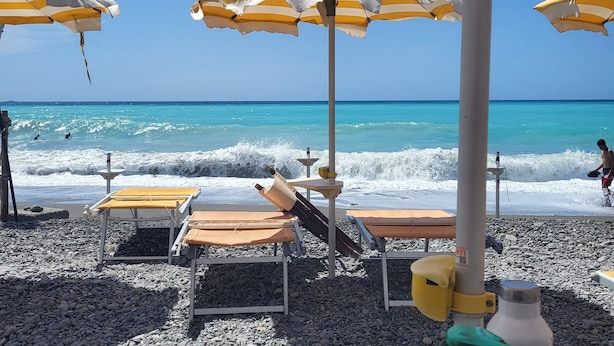 A beach with striped umbrellas, lounge chairs, and a rocky shoreline. - Residenza Villa Genua (Bordighera)