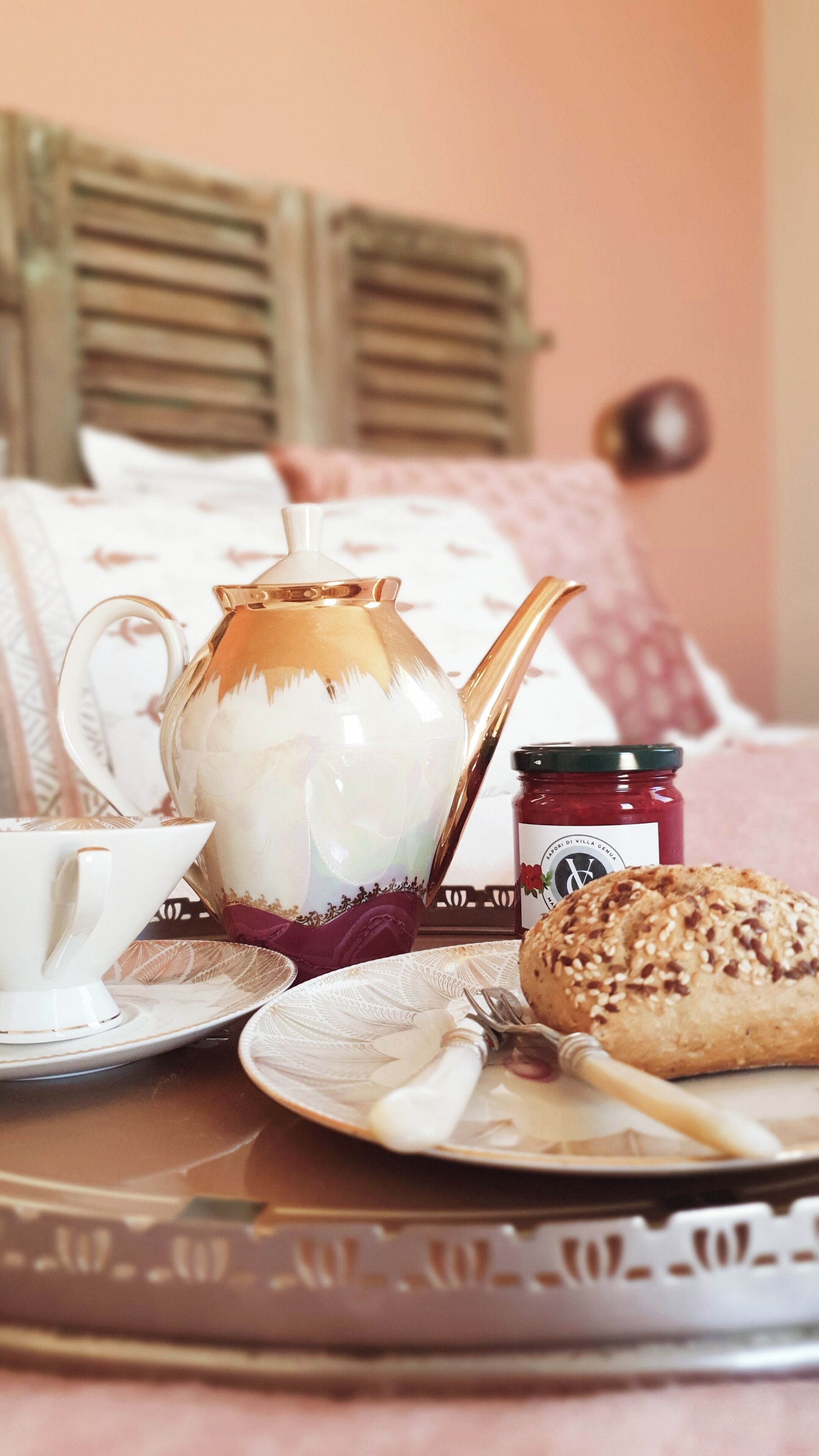 A tray with a teapot, a cup, a jar of jam, and a slice of bread on a table.