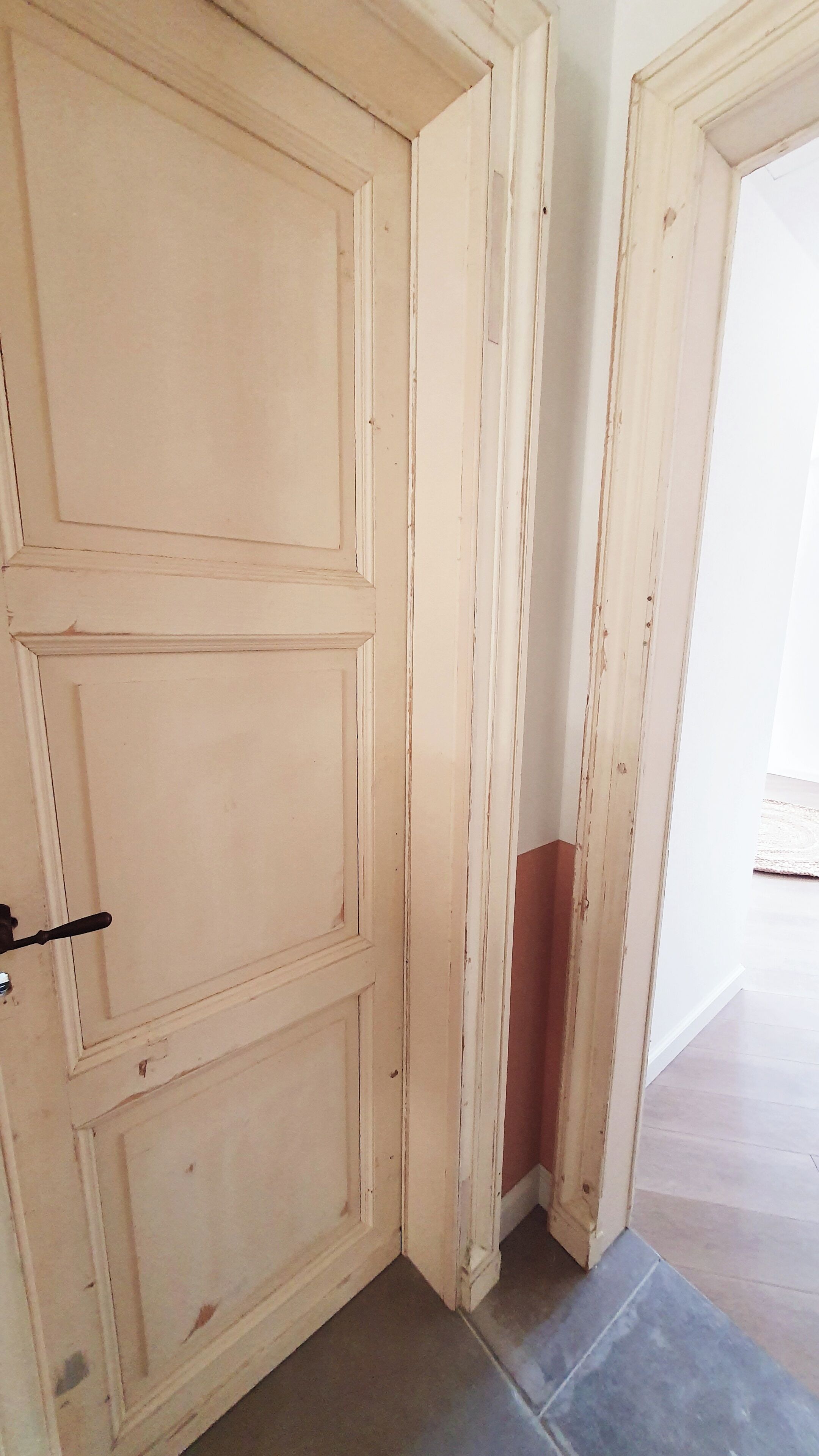 A closed wooden door with a simple handle, adjacent to a partially open door revealing a red wall and a tiled floor.
