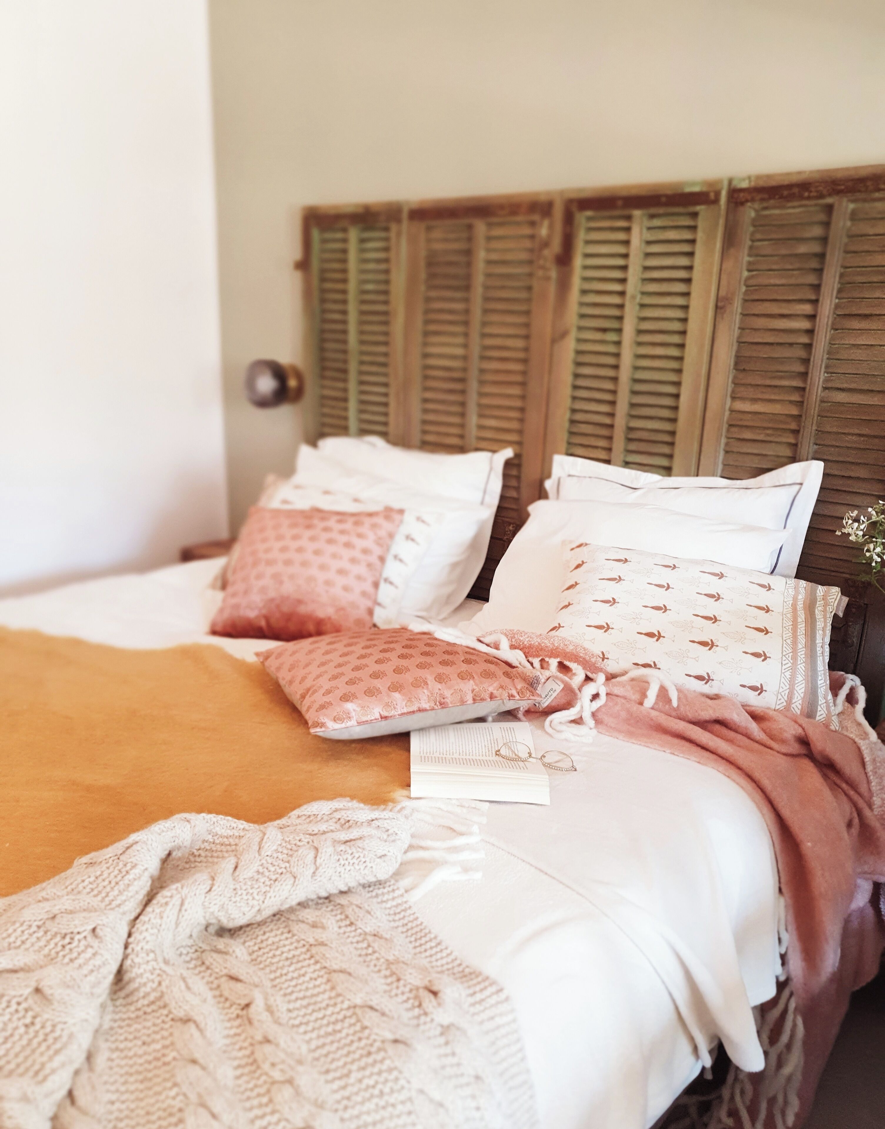 A neatly made bed with patterned pillows, a knitted blanket, and a wooden headboard.