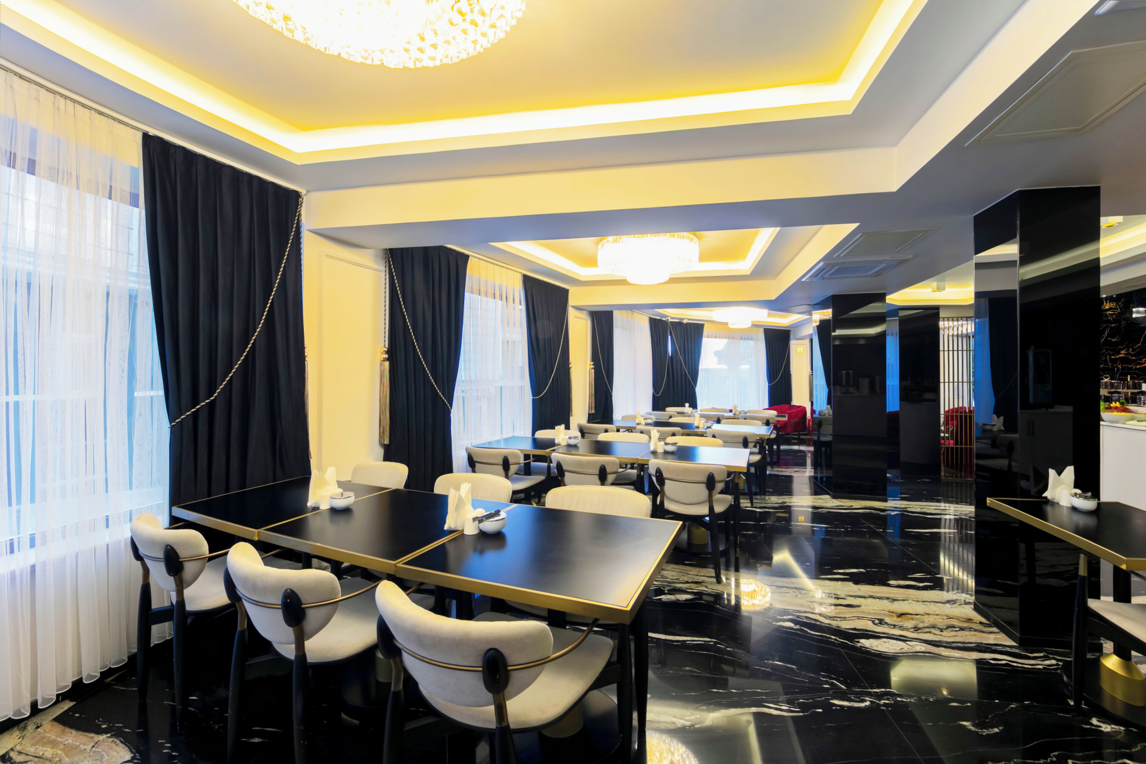Een restaurant in een hotel met meerdere tafels en stoelen, een kroonluchter en een modern interieur.