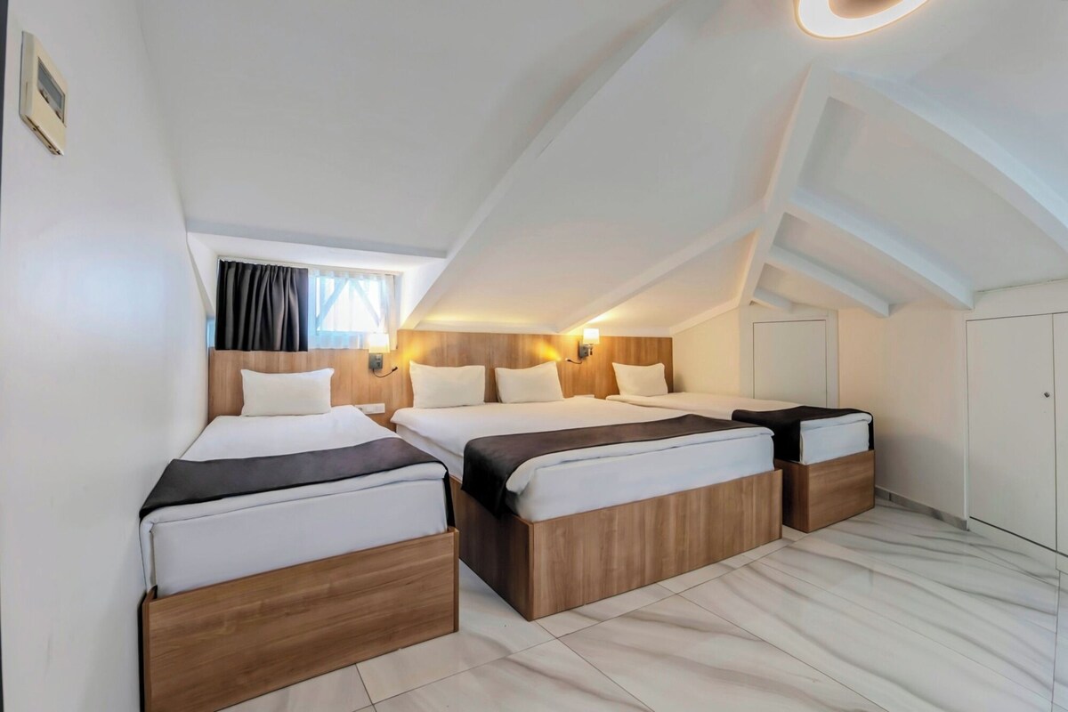 A bedroom with two beds, wooden headboards, white bedding, a window with curtains, and a ceiling with a skylight.
