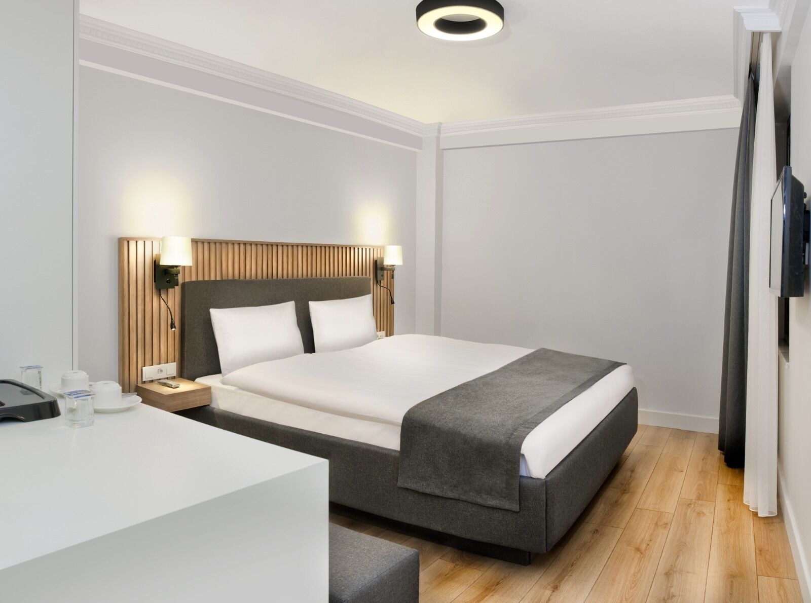 Een moderne hotelkamer met een bed, nachtkastjes, een bureau en een flatscreen televisie.