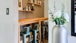 A dining area with a wooden table and chairs, a shelf with framed pictures, and a vase with white flowers. - This apartment is a 2 bedroom(s), 1 bathrooms, located in Berkley, MI. (Berkley)