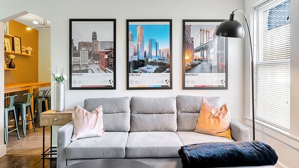 A modern living room with a grey sofa, a coffee table, and a framed cityscape artwork on the wall. - This apartment is a 2 bedroom(s), 1 bathrooms, located in Berkley, MI. (Berkley)