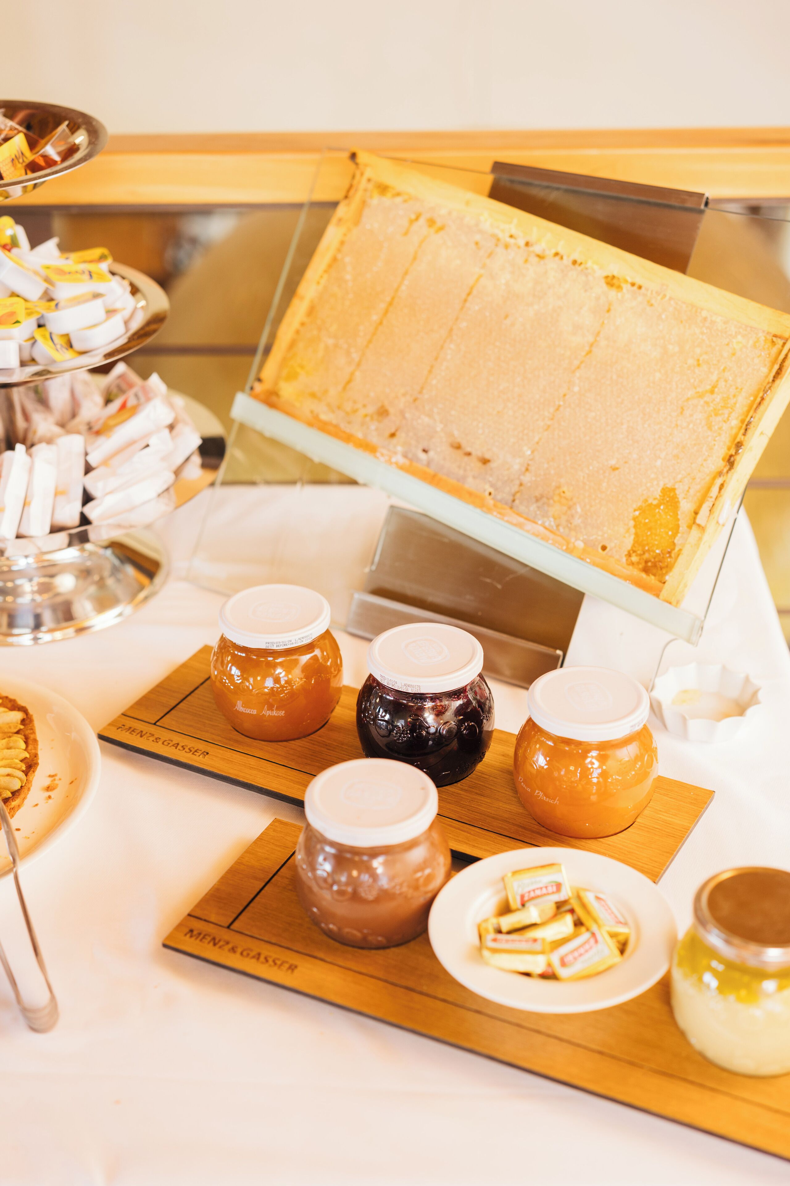 Une table de buffet proposant une variété d’aliments, notamment des pots de miel, des pâtisseries et un présentoir avec des rayons de miel.