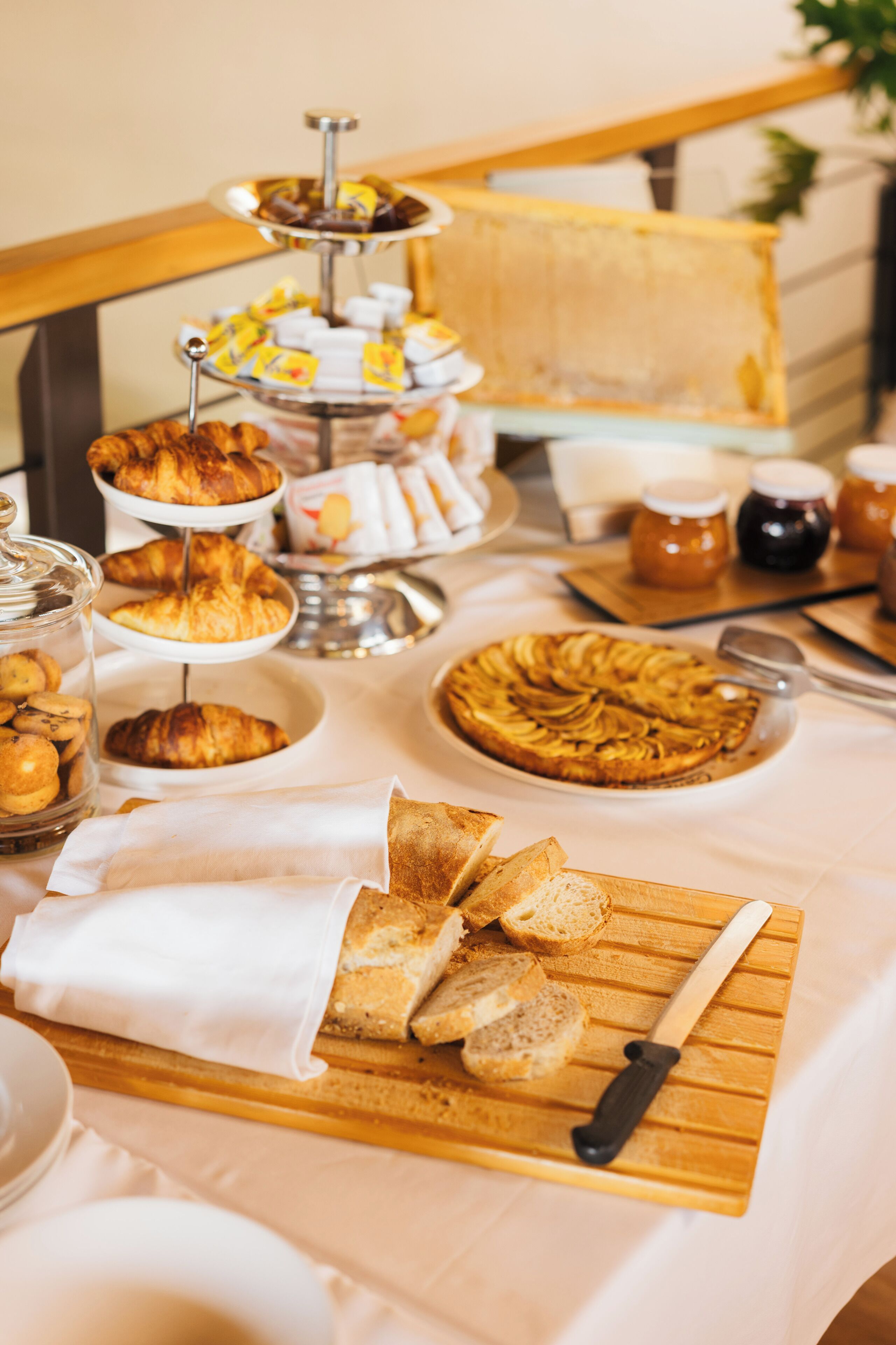 A breakfast buffet with various pastries, bread, and a fruit tart on a wooden board.