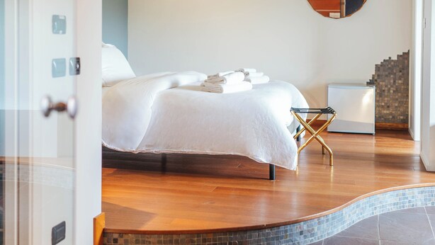 Une chambre à coucher moderne avec un lit, un petit tabouret et un miroir au mur.